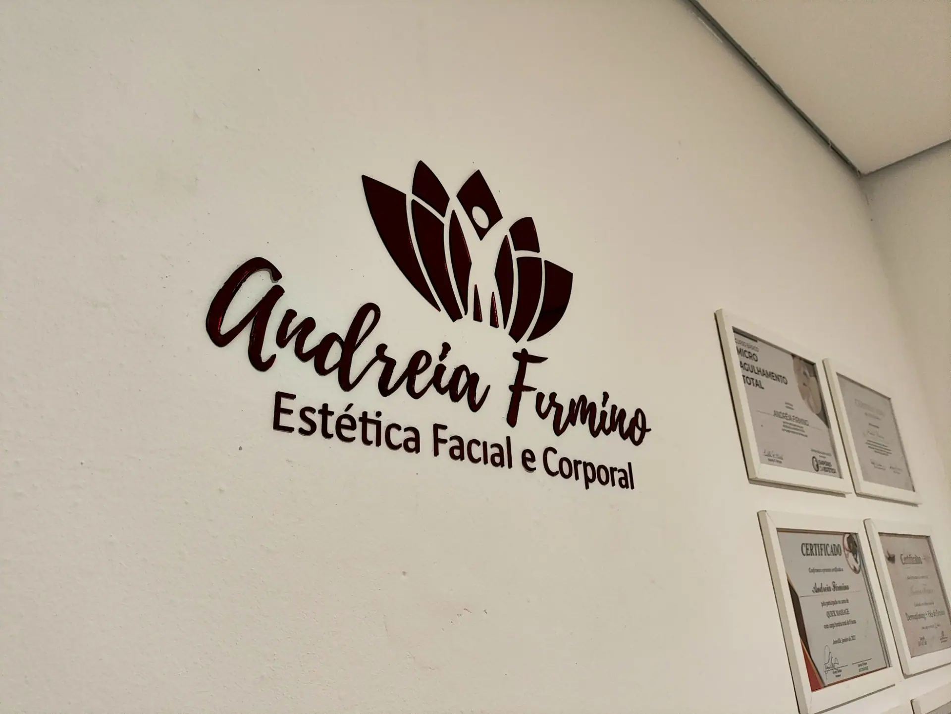 Letreiro "Andreia Firmino, Estética Facial e Corporal" na parede do espaço, ao lado dos certificados emoldurados